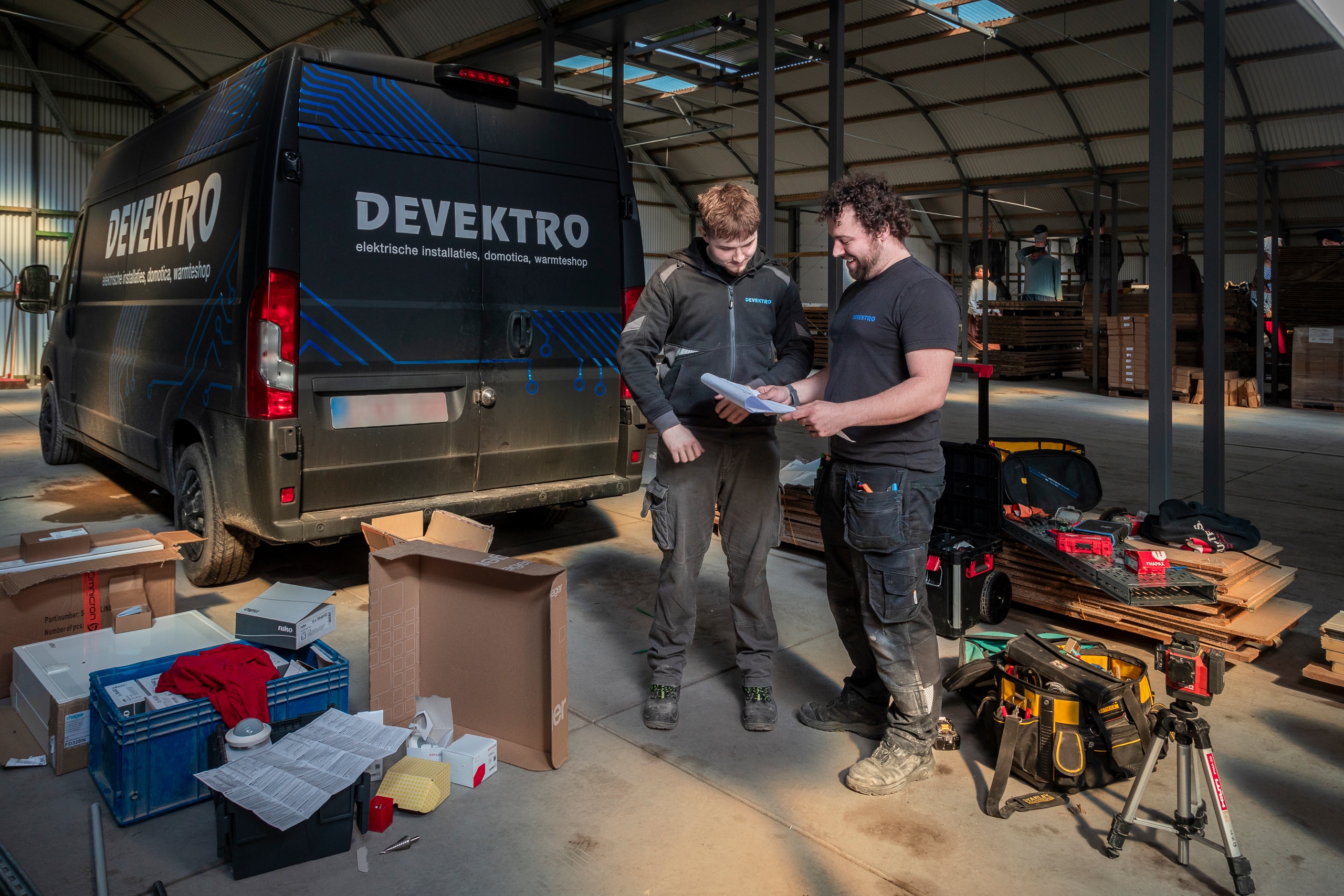 Twee mannen die voor een camionette staan met elektricien gereedschap, klaar om te werken.